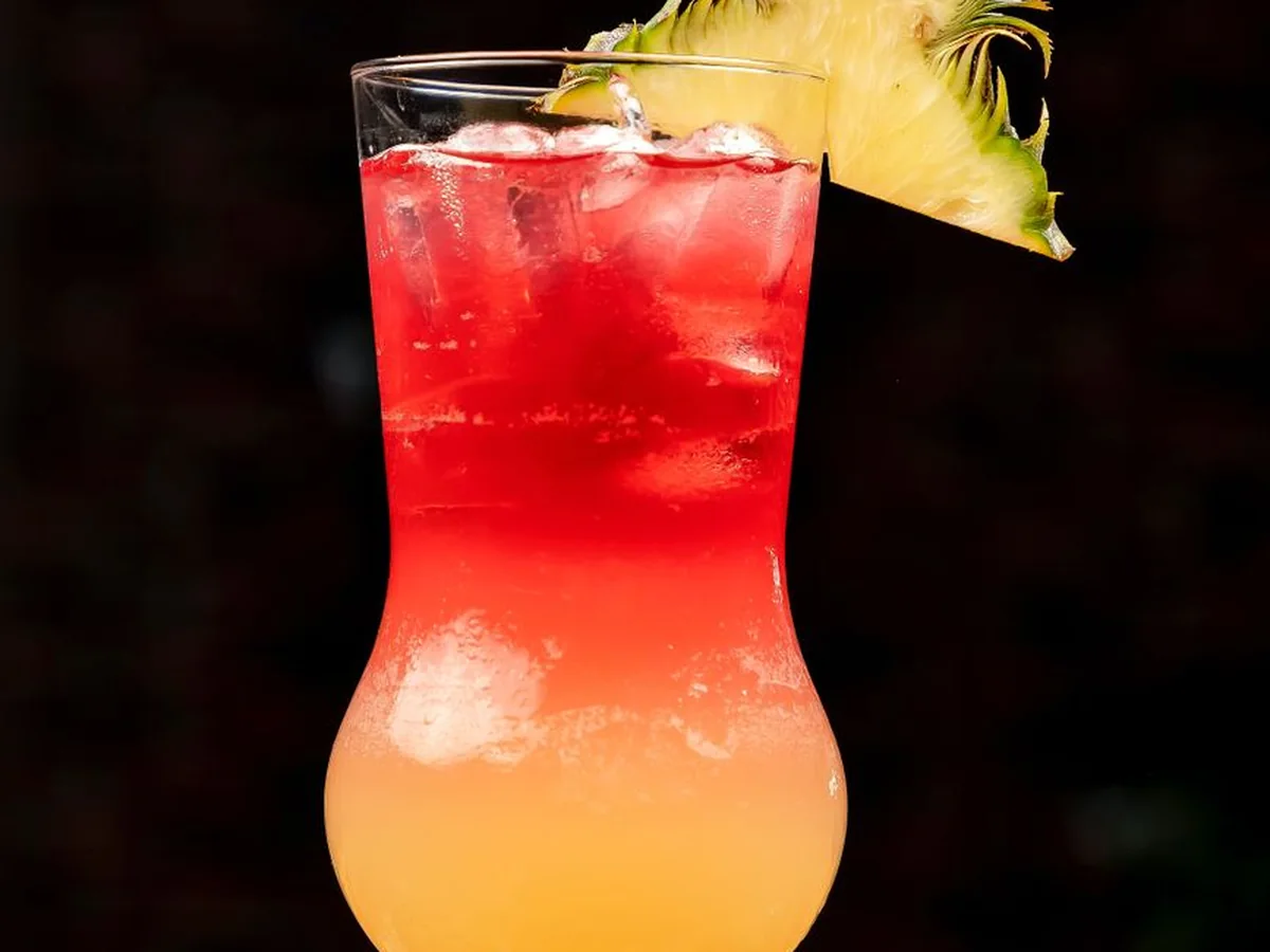 A tropical layered cocktail garnished with a pineapple wedge, condensation on the glass (representative photograph of a tropical cocktail, not Ka Moana's own bar)