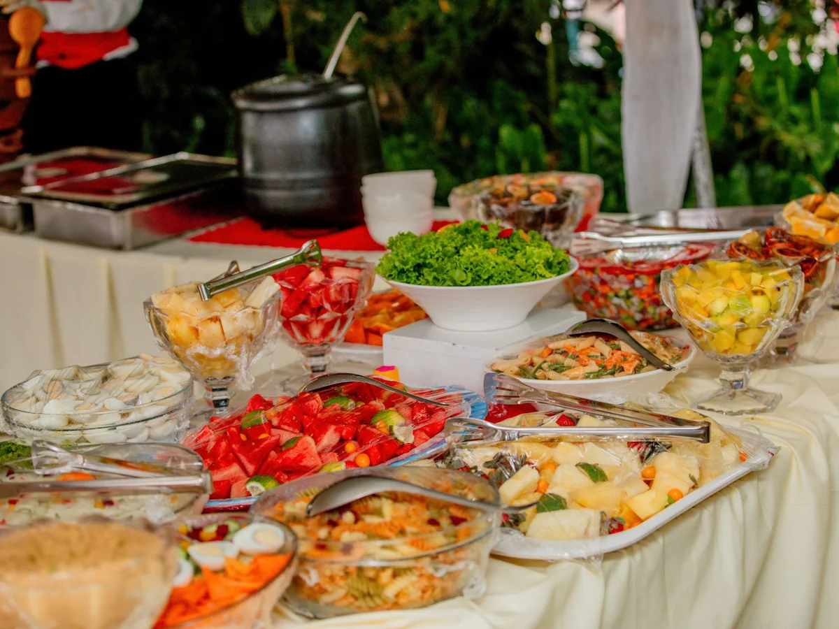 An outdoor buffet table spread with salads, fruit and mixed dishes in serving trays (representative photograph of a buffet-style spread, not Ka Moana's own table)