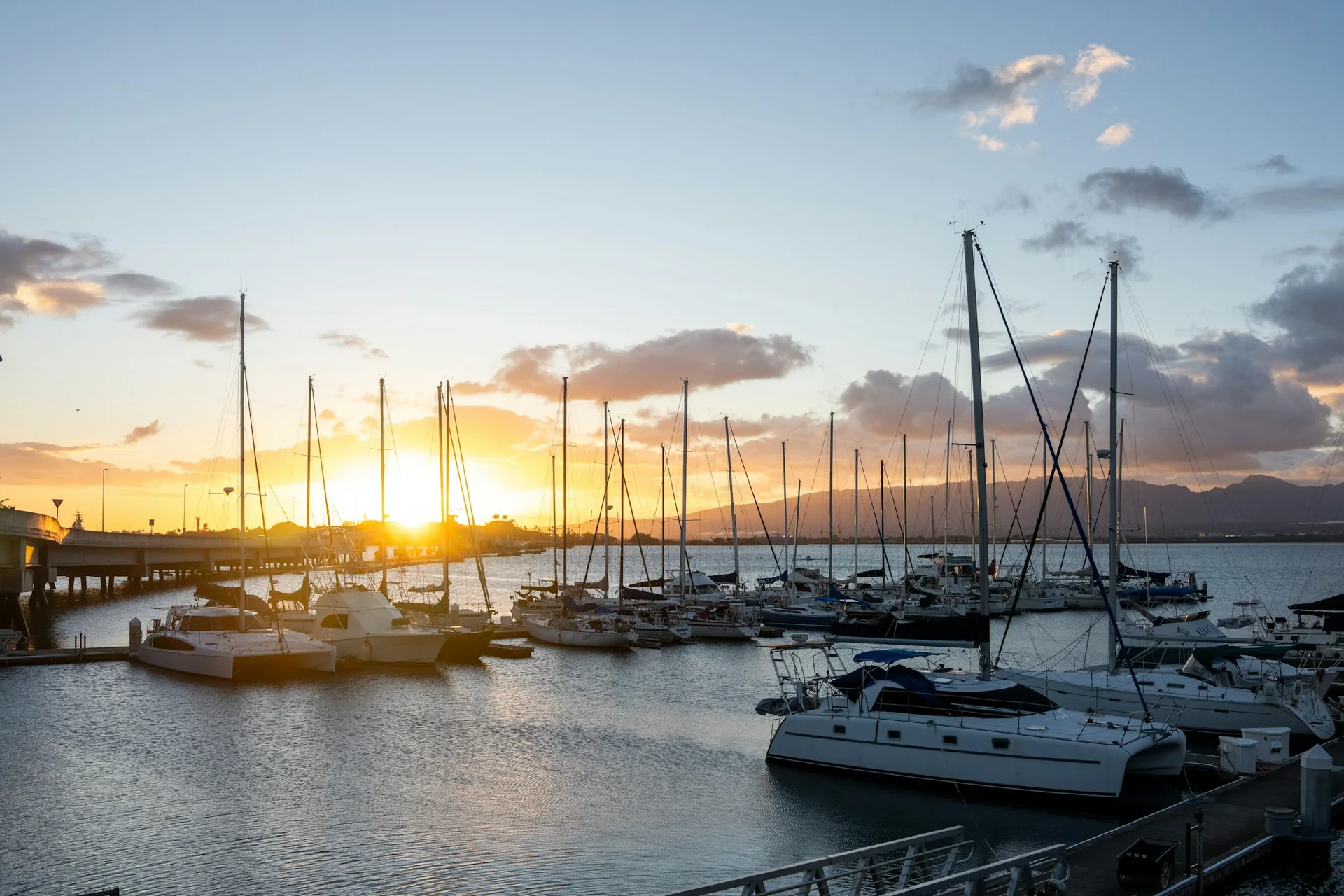 A Hawaiian marina at sunset, sailboat masts silhouetted against a gold and pink sky over the water (representative photograph of a Honolulu-area harbour at sunset, not Ka Moana's own lawn)
